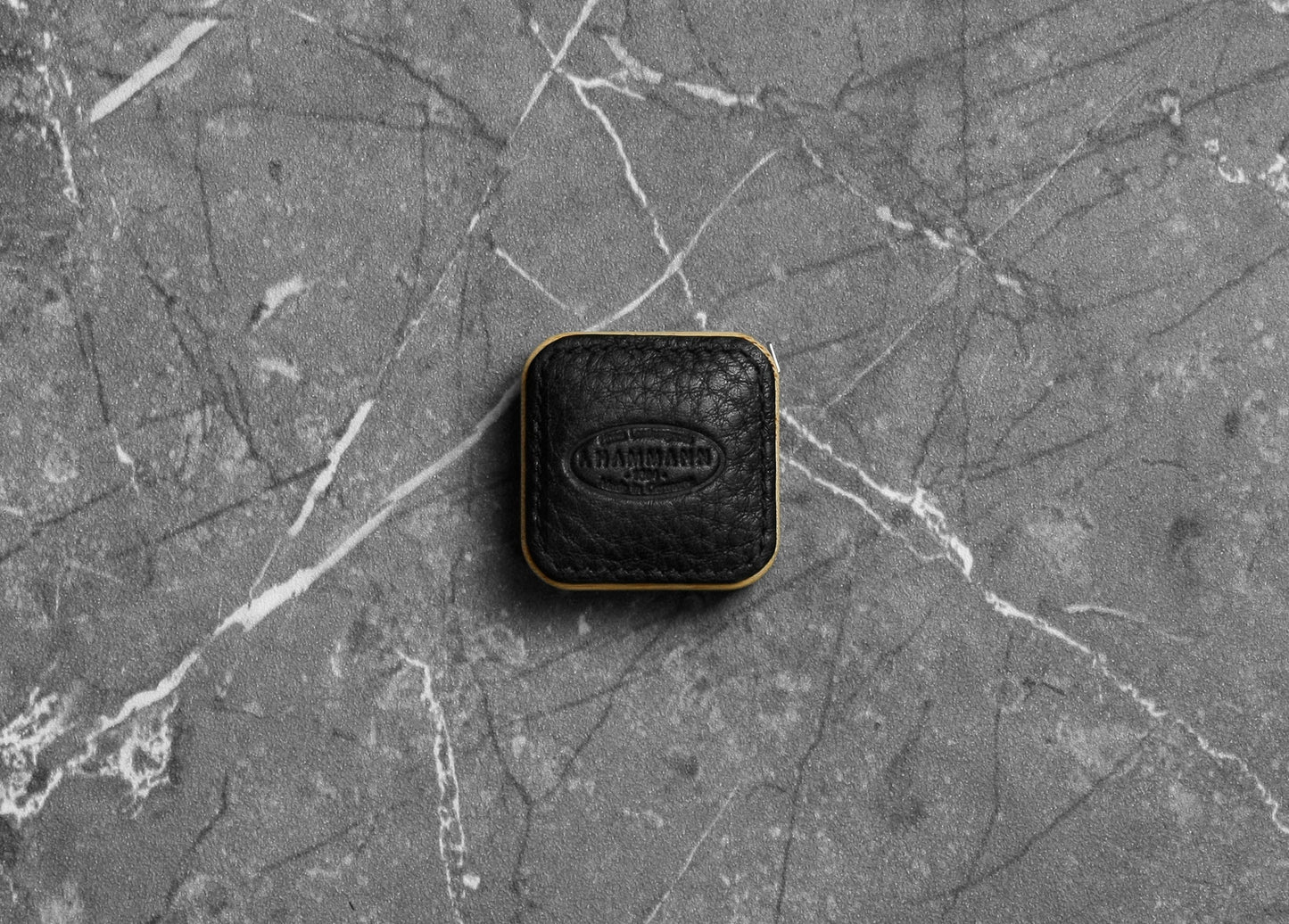 Top-down photograph of the F. Hammann 5205 Black Chervo Leather Tape Measure resting on grey marble.