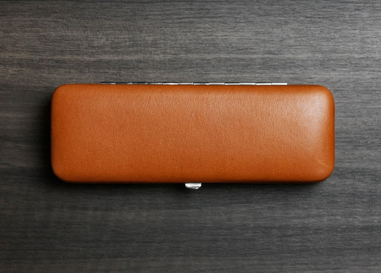 Top-down view of the F. Hammann 3883 Coxorange leather case, showcasing its flat, pocket-friendly footprint on a textured dark wood surface.