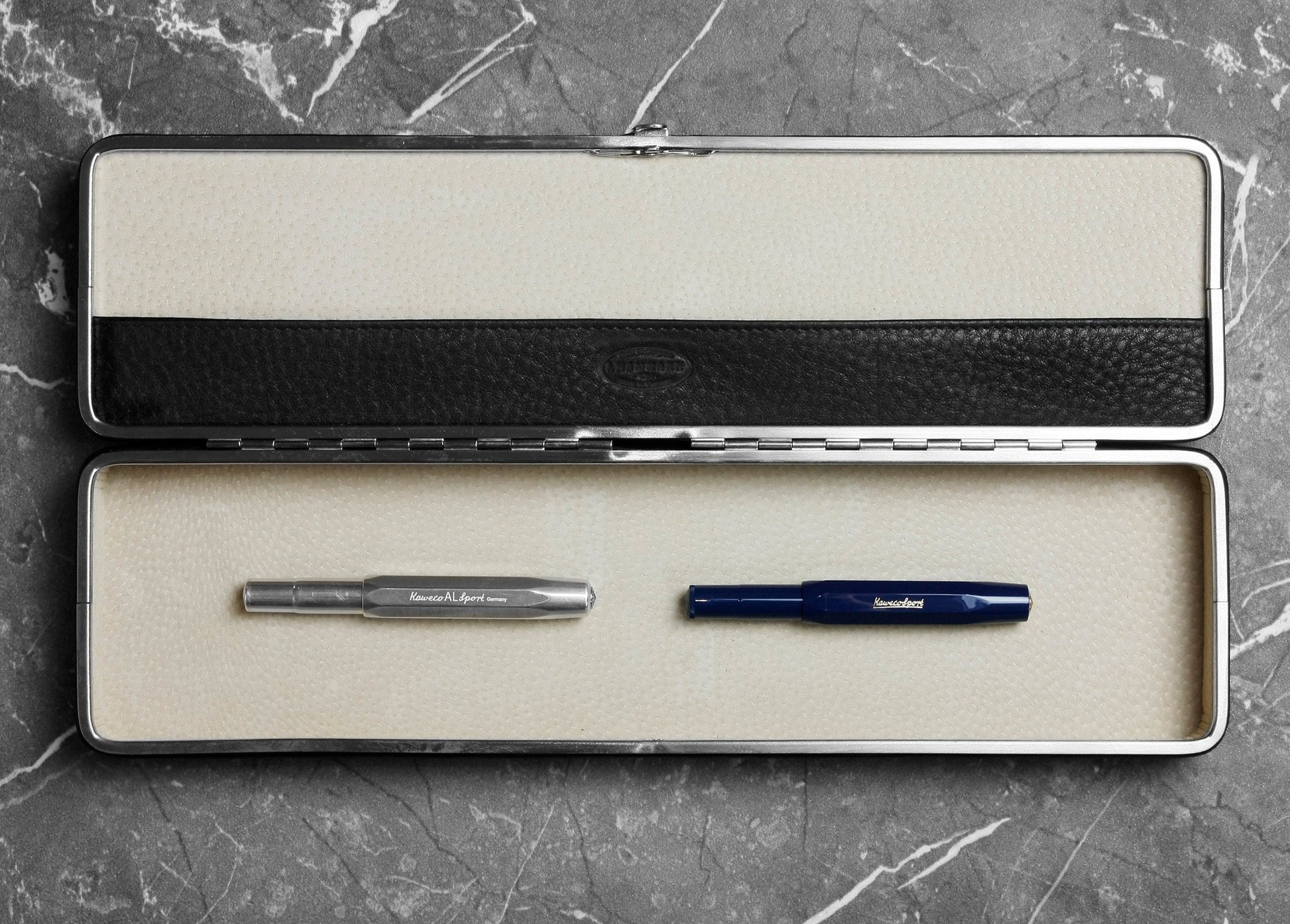 Open F. Hammann 3976 black leather case on marble, revealing a beige suede interior holding two Kaweco fountain pens.