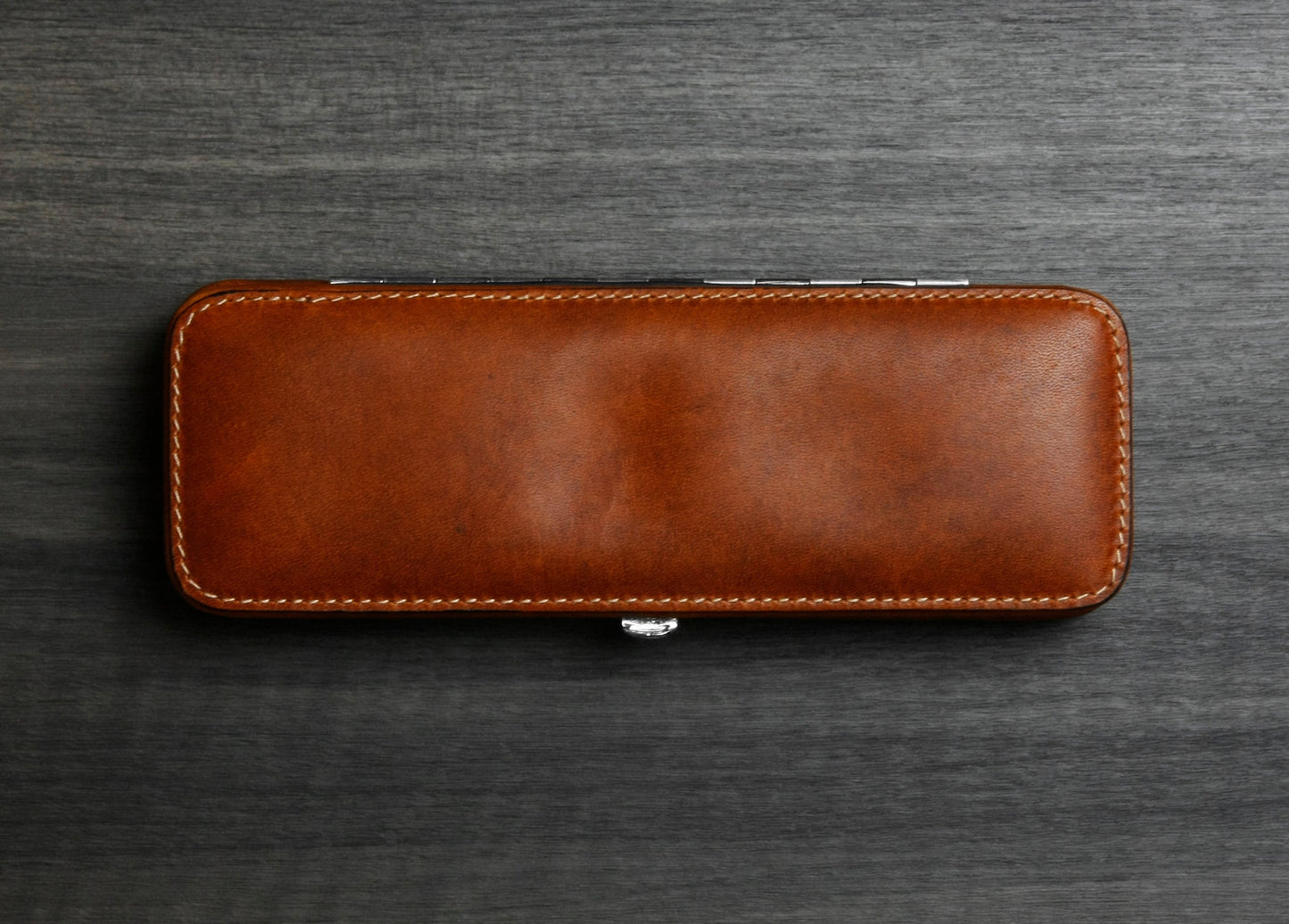 Top-down view of the F. Hammann 3983 Coxorange leather 3-pen case resting flat on a textured dark wood surface.