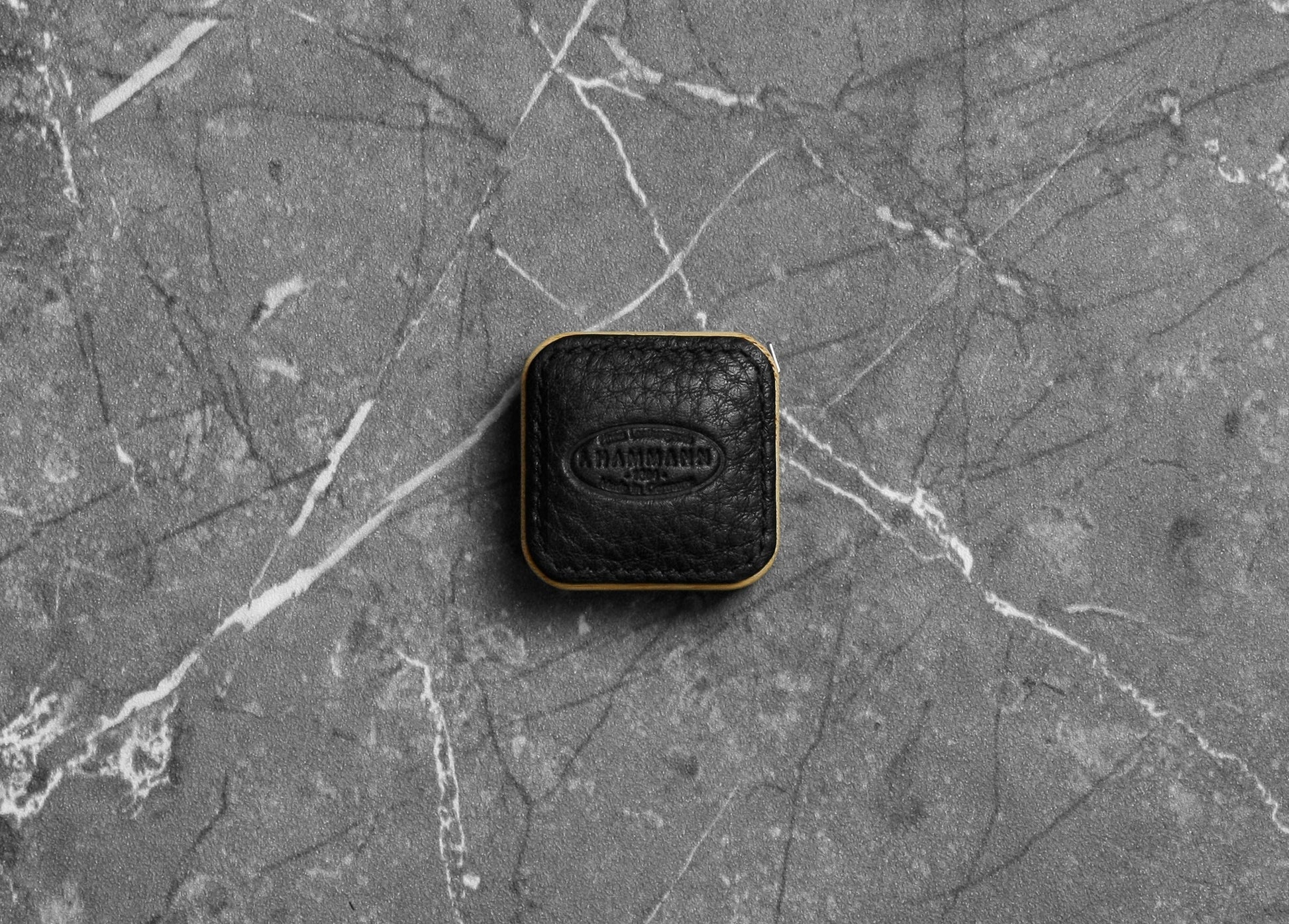 Top-down photograph of the F. Hammann 5205 Black Chervo Leather Tape Measure resting on grey marble.